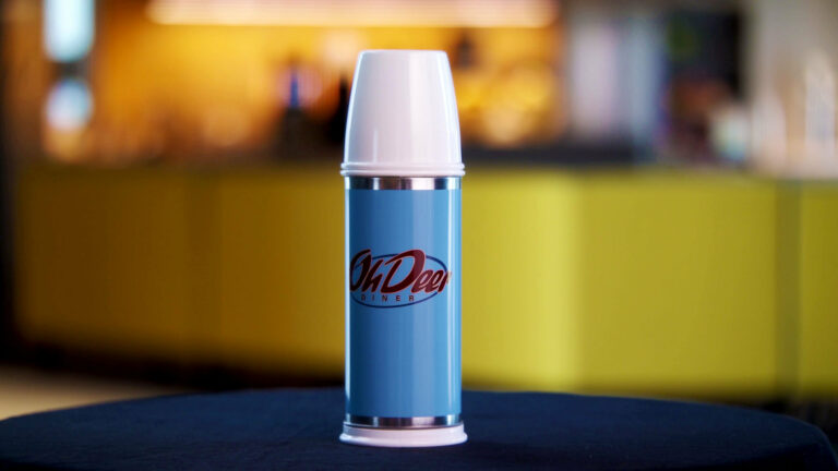 Light blue Oh Deer Diner thermos on the table. Colorful blurry background.